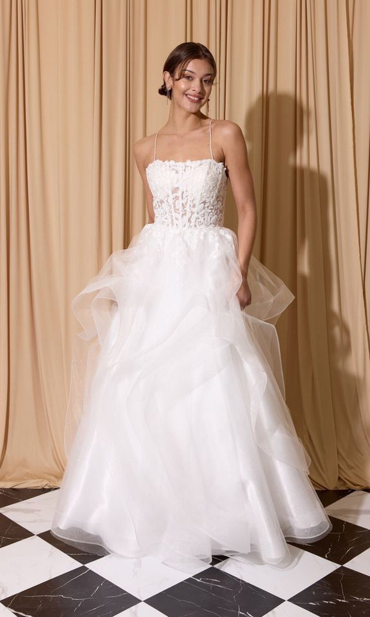 A woman wears the Eureka EK167 long prom dress, featuring a white strapless ball gown with a floral lace embroidered corset and layered tulle A-line skirt, standing on a black and white checkered floor against beige curtains.